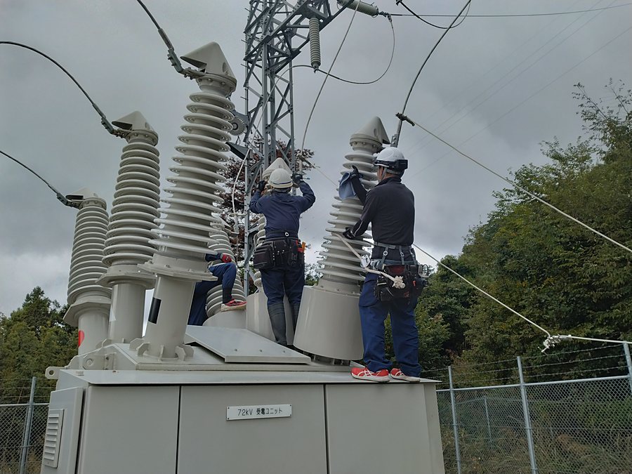 72kVの受電設備の上に立ち、高圧線の端末を扱う2人の作業員