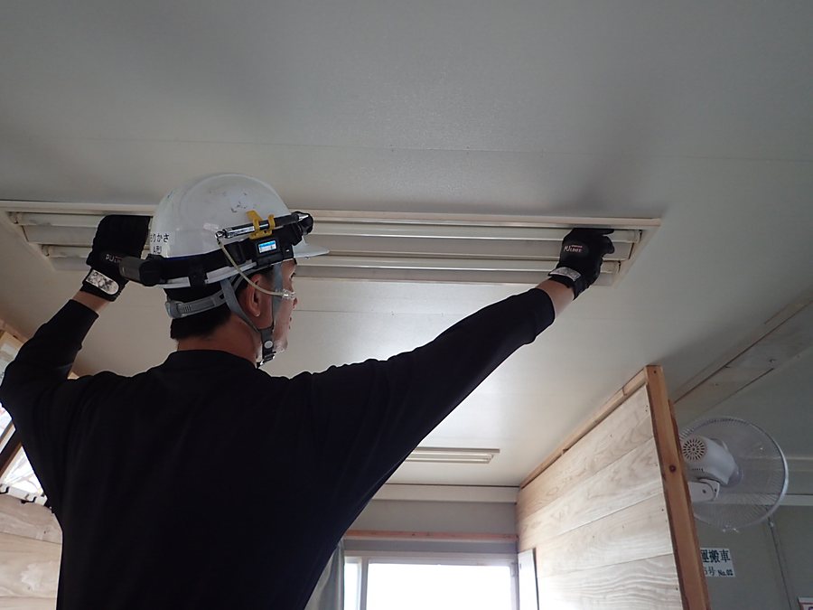室内の天井に照明器具を取り付けている作業員