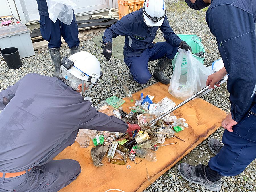 回収したごみを机の上に広げて缶・びんなどに分別する社員